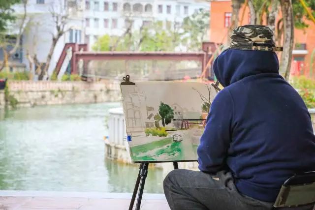 小桥流水的一侧,一位民间画家落笔画下了古镇的绿美景象。 图片